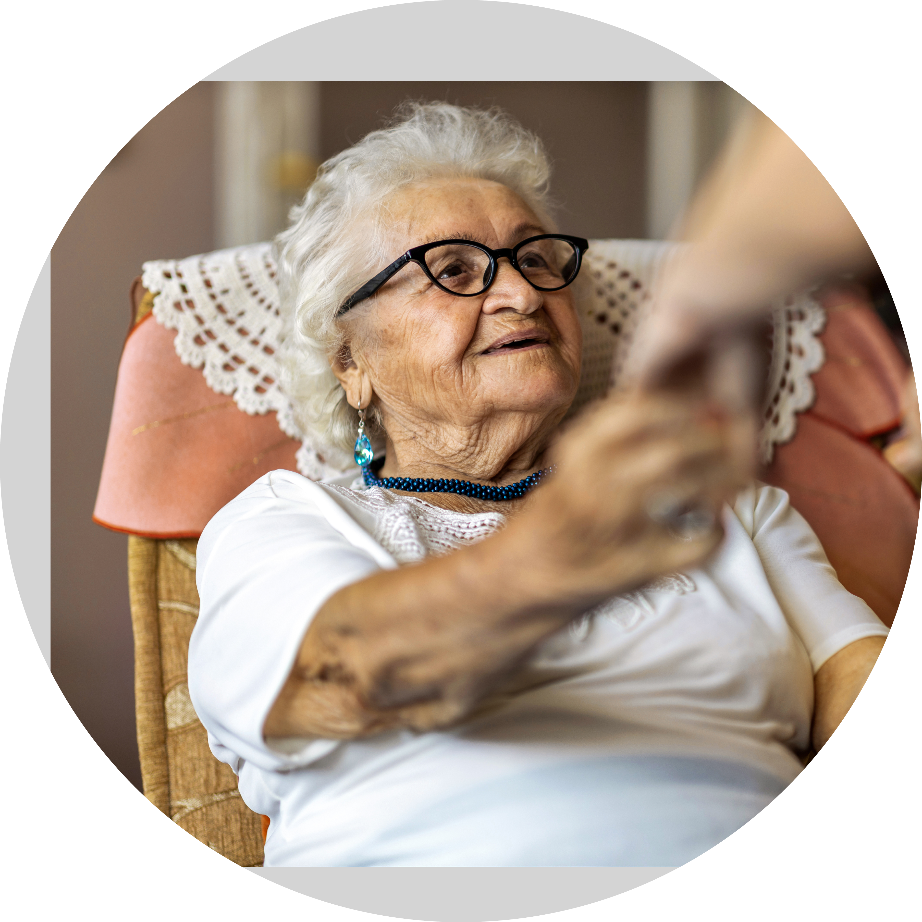 Female home carer supporting old woman to stand up from the armchair at care home