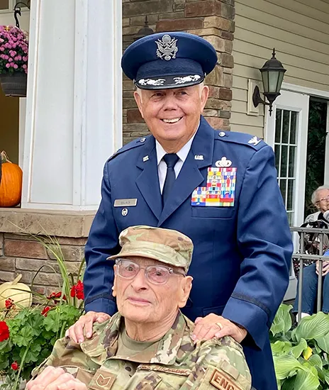 Decorated serviceman pushing another elderly veteran in a wheelchair