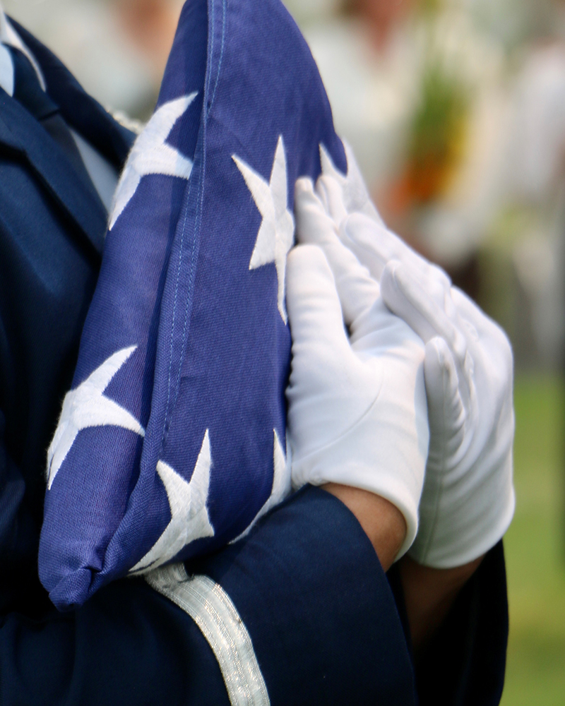 Closeup, male in blue uniform carrying folded American flag