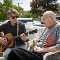 Younger gentleman playing guitar for older gentleman